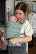 Teal floral baby carrier with pocket, holding a sleeping newborn