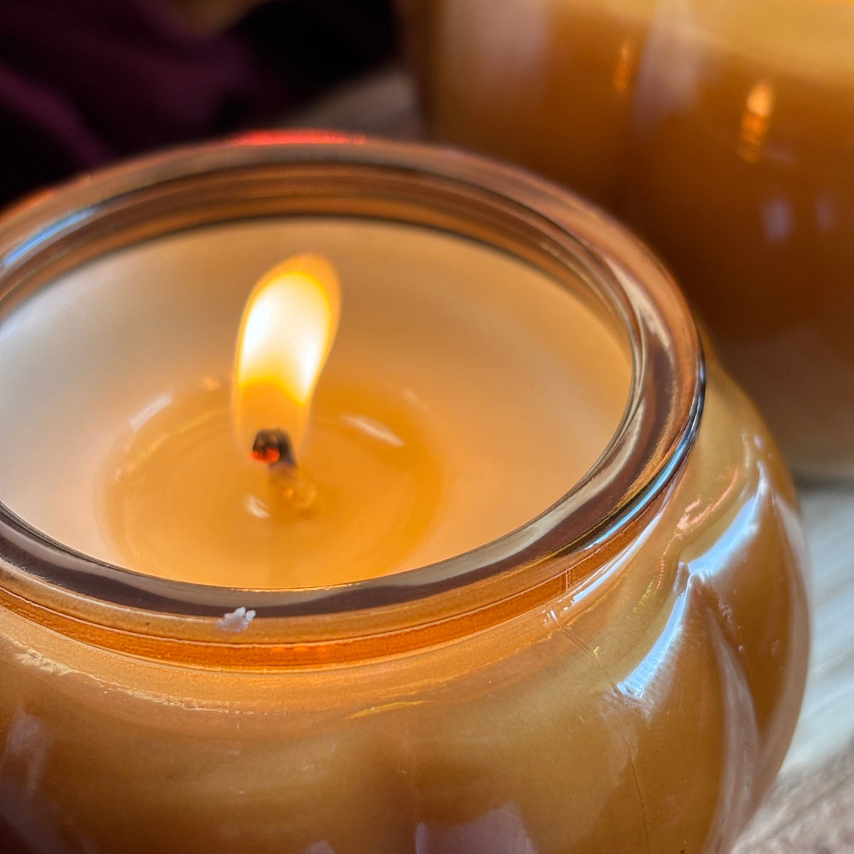 Close-up of amber soy candle flame inside round glass jar, with white wax top