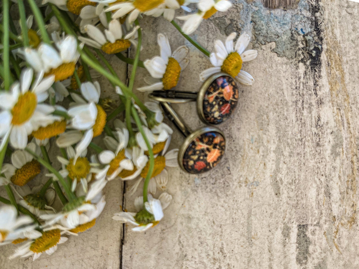 Close-up of round floral leverback earrings with orange and blue botanical print, bronze tone.