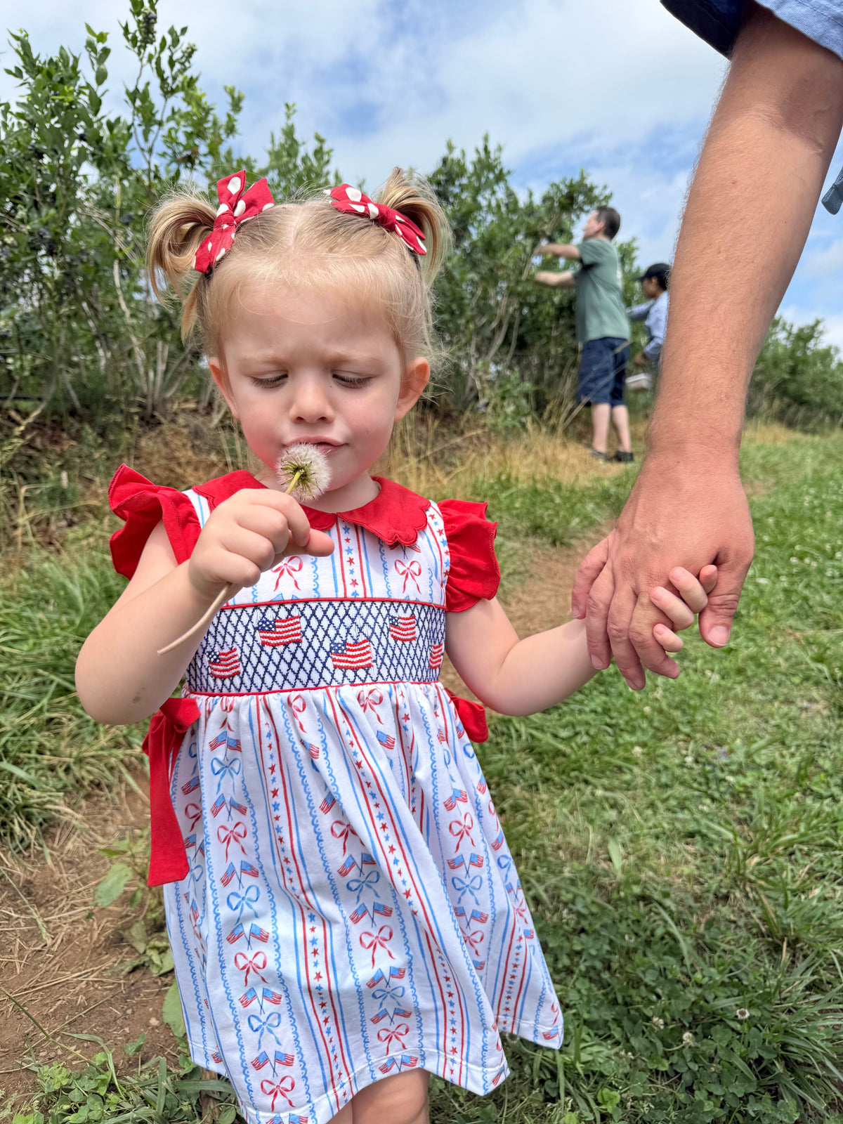 Girls patriotic smocked dress worn front, red shoulder bows and blue striped skirt
