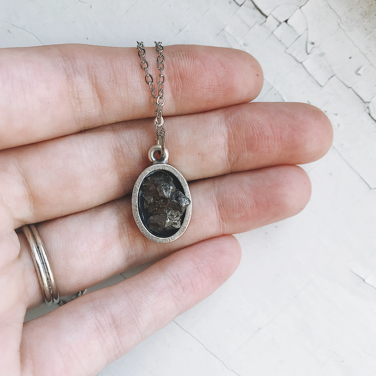 Oval meteorite pendant necklace held in hand, dark stone in silver oval bezel