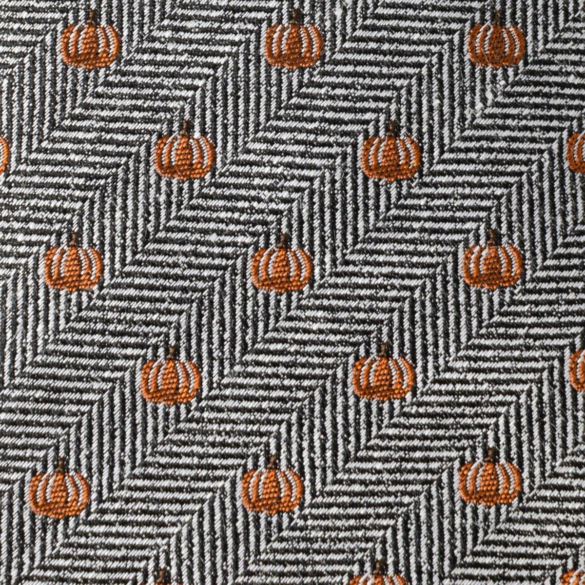Close-up herringbone tie fabric with small orange pumpkin icons on gray background.