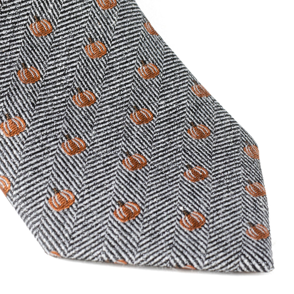 Orange pumpkin pattern on gray herringbone tie fabric, showing stitched edge near tip.
