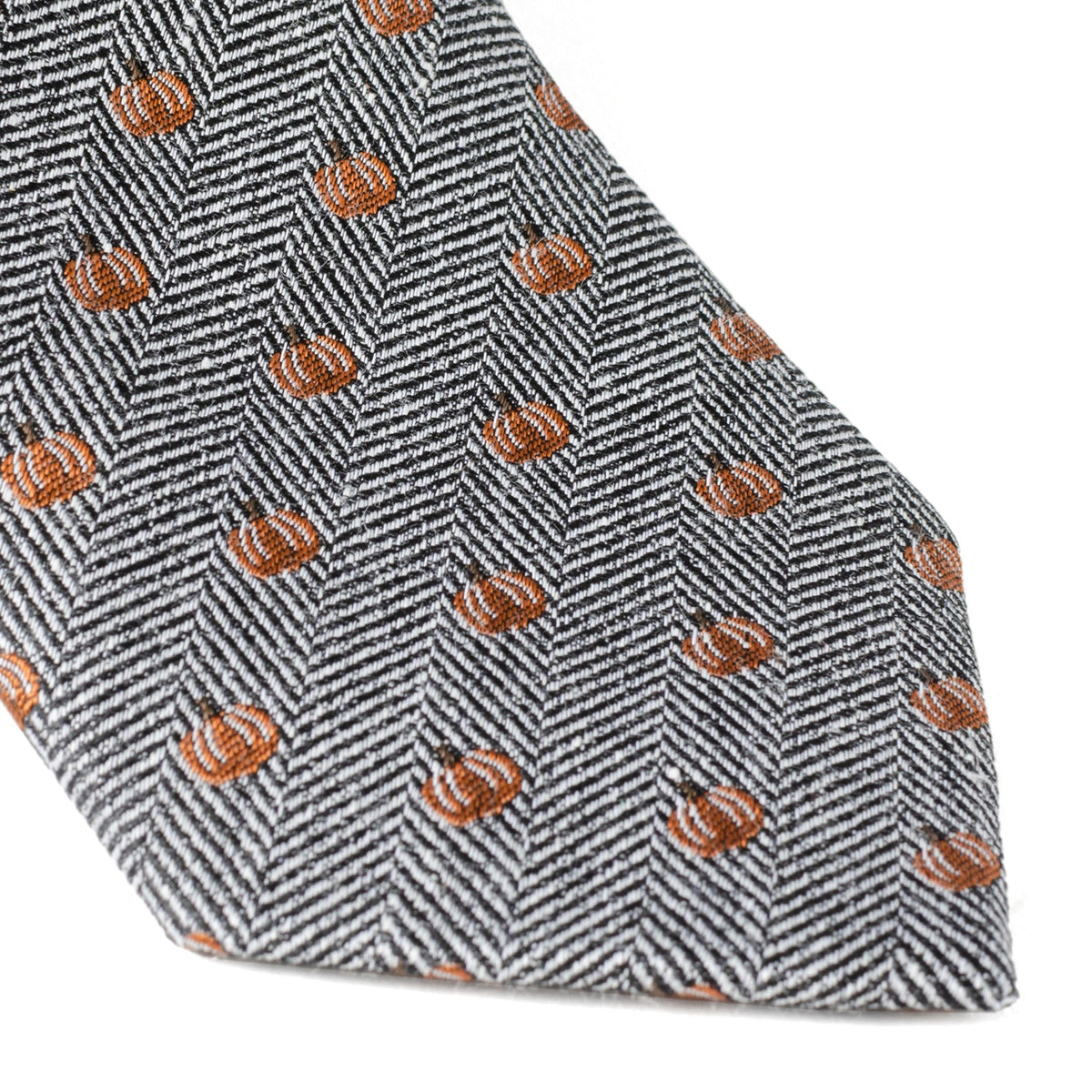 Orange pumpkin pattern on gray herringbone tie fabric, showing stitched edge near tip.