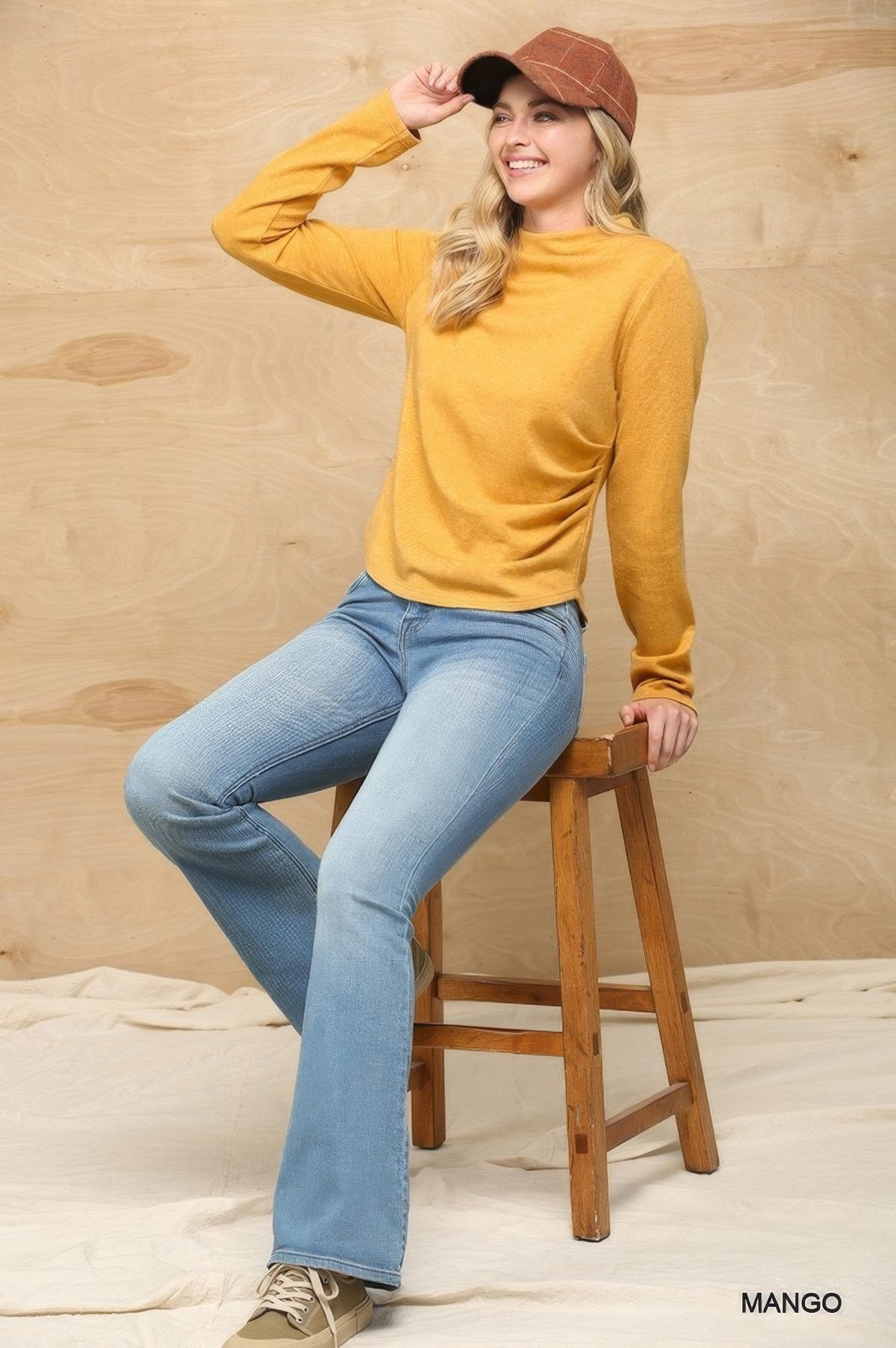 Women’s mustard mock neck knit top with long sleeves and side ruching, seated.