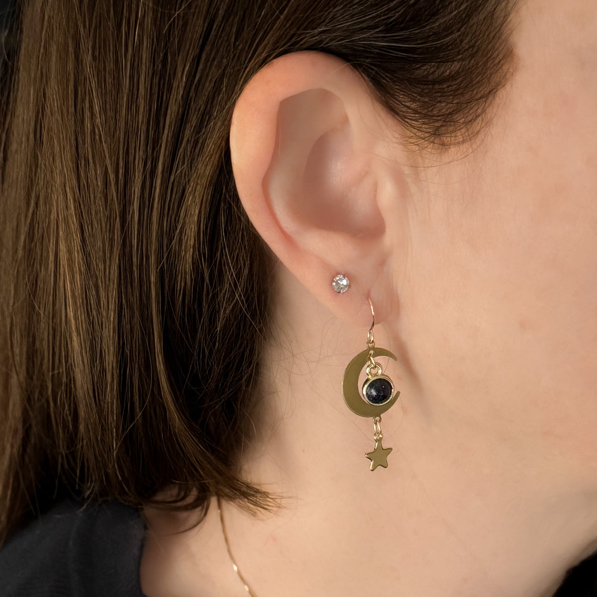 Model wearing gold crescent moon earrings with dark blue stone and star charm