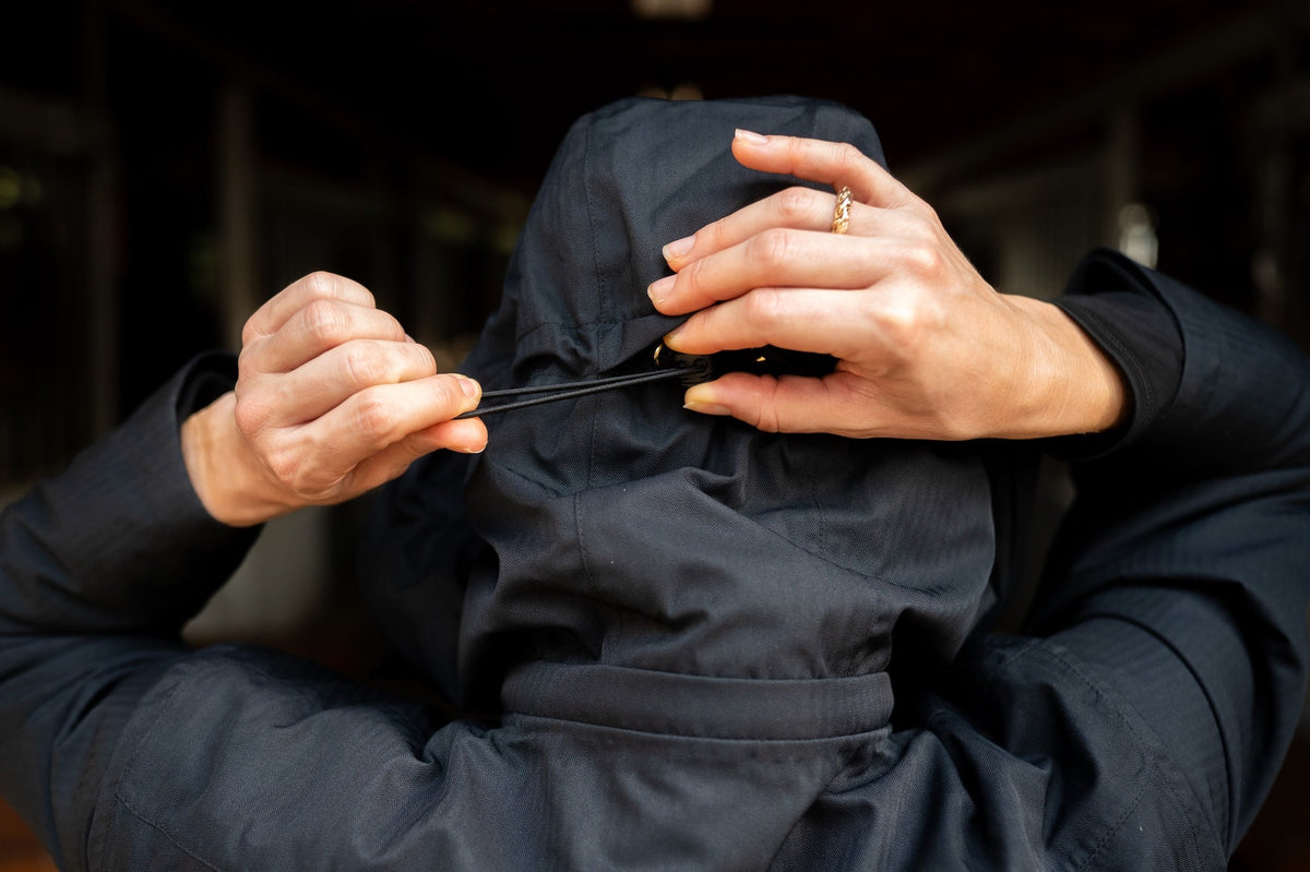Close-up of dark hooded insulated jumpsuit, hands adjusting the front drawstring