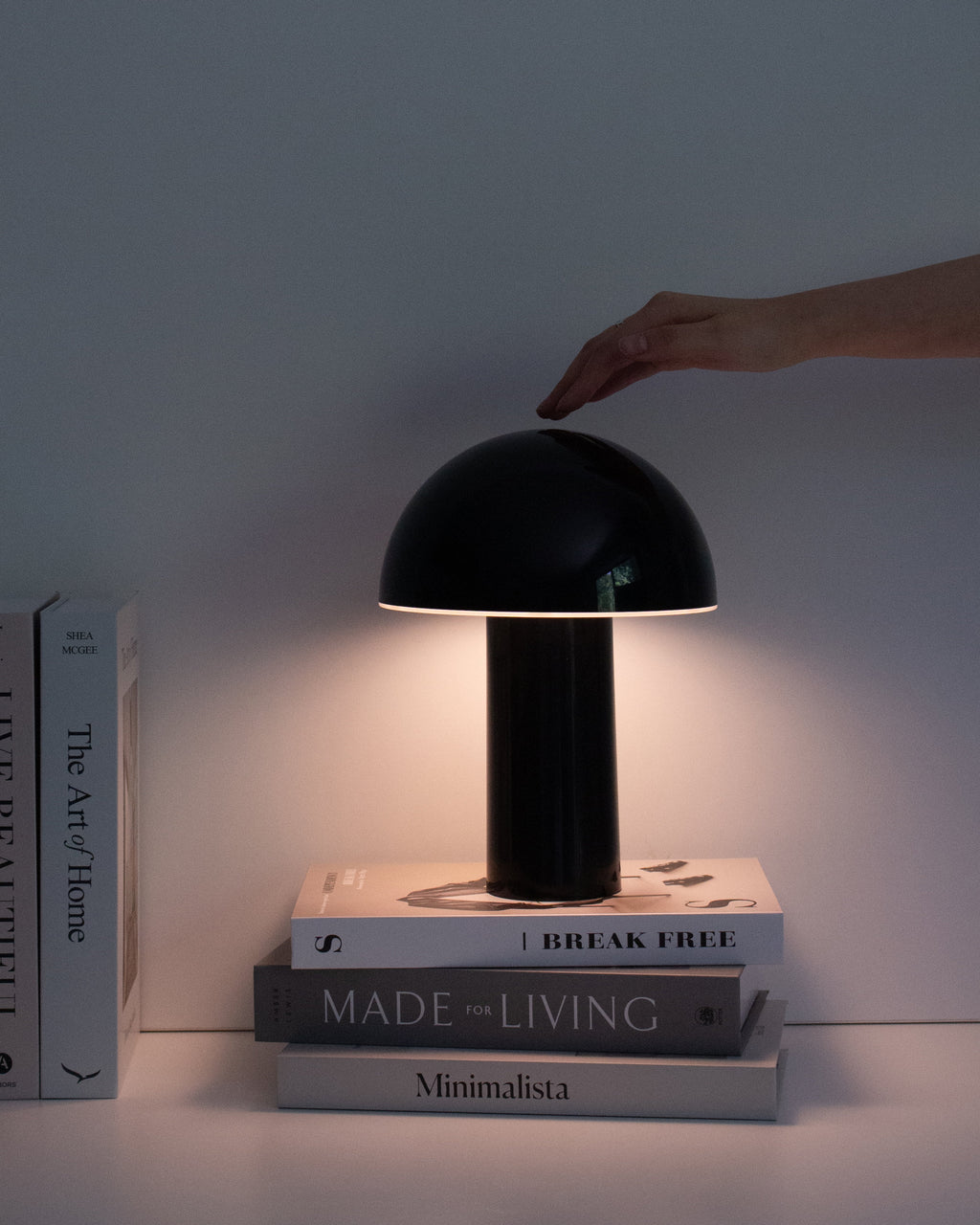 Black portable lamp with dome shade on stacked books, warm light glow