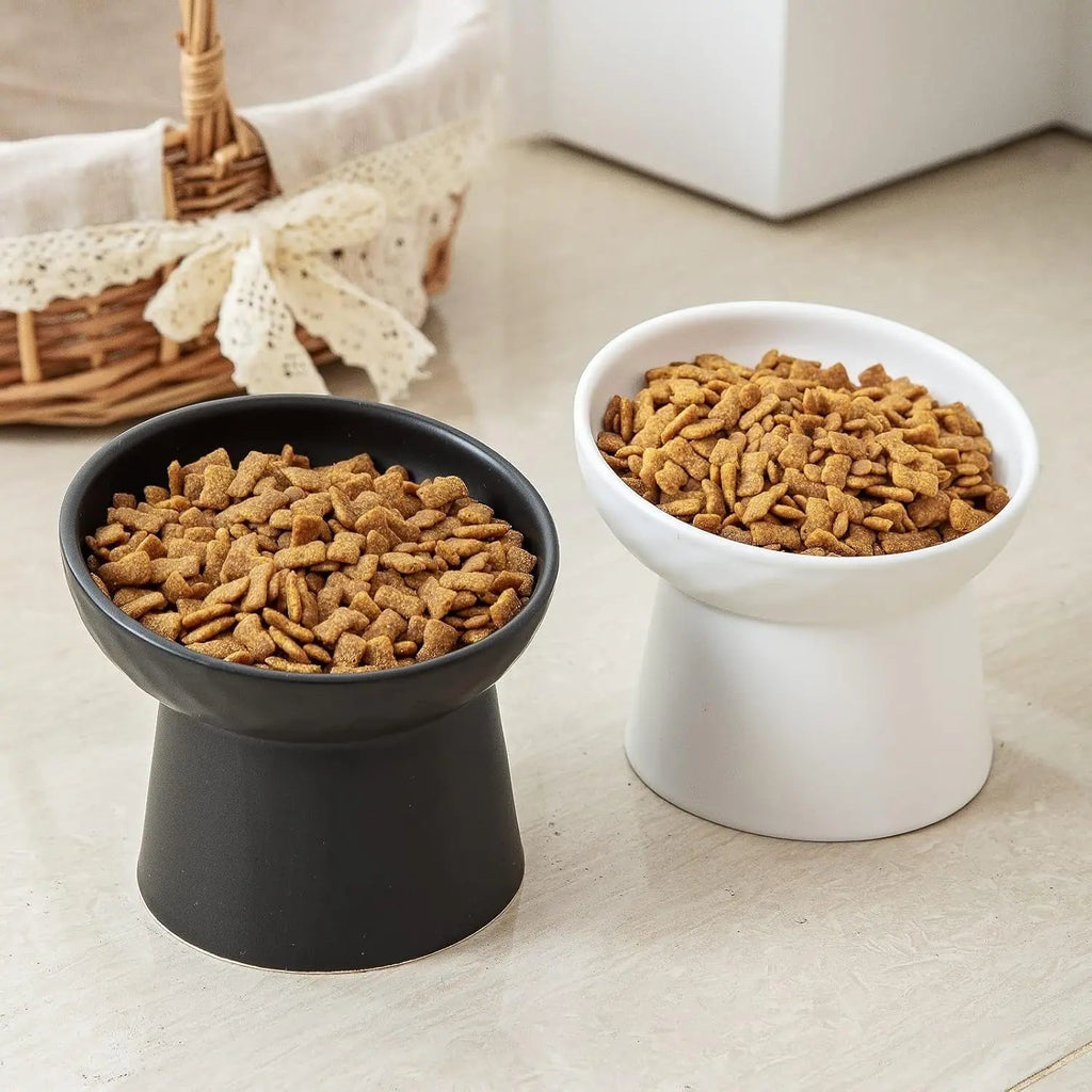 Pair of raised tilted ceramic cat bowls, black and white, filled with kibble