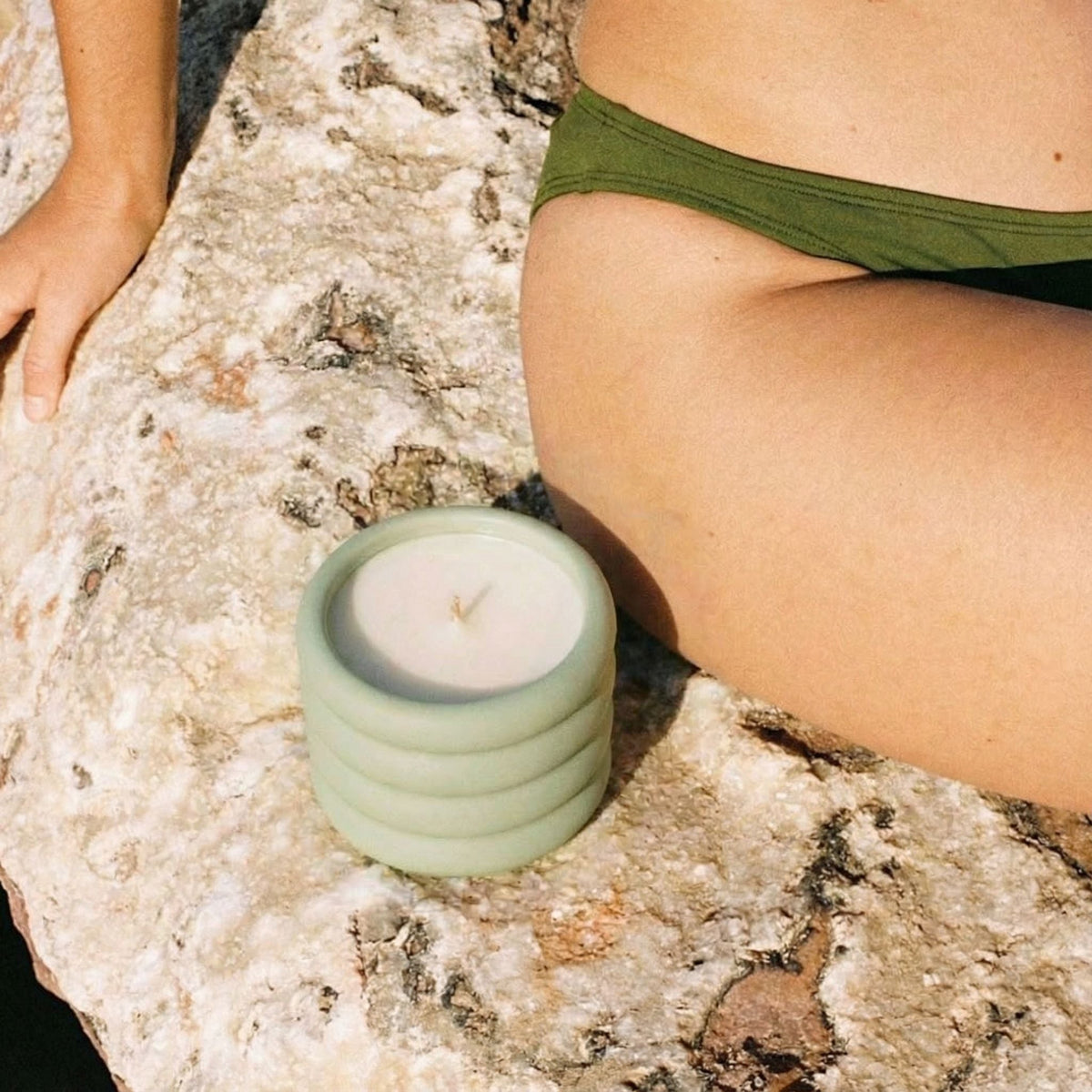 Green ridged ceramic soy wax candle jar with lit wick on stone