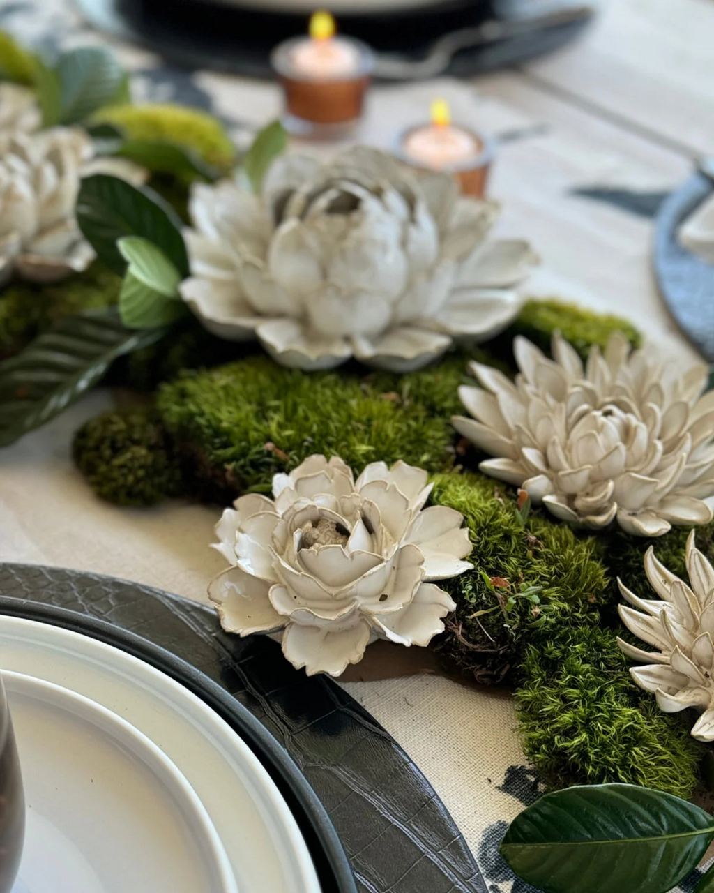 Cream ceramic flower wall art with layered petals on mossy floral display