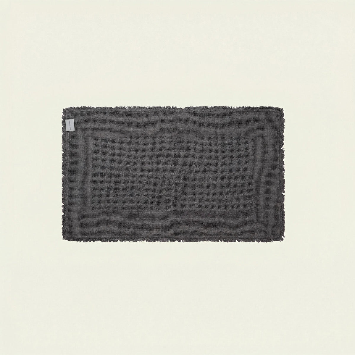 Dark charcoal plush bath mat with textured surface and small tag