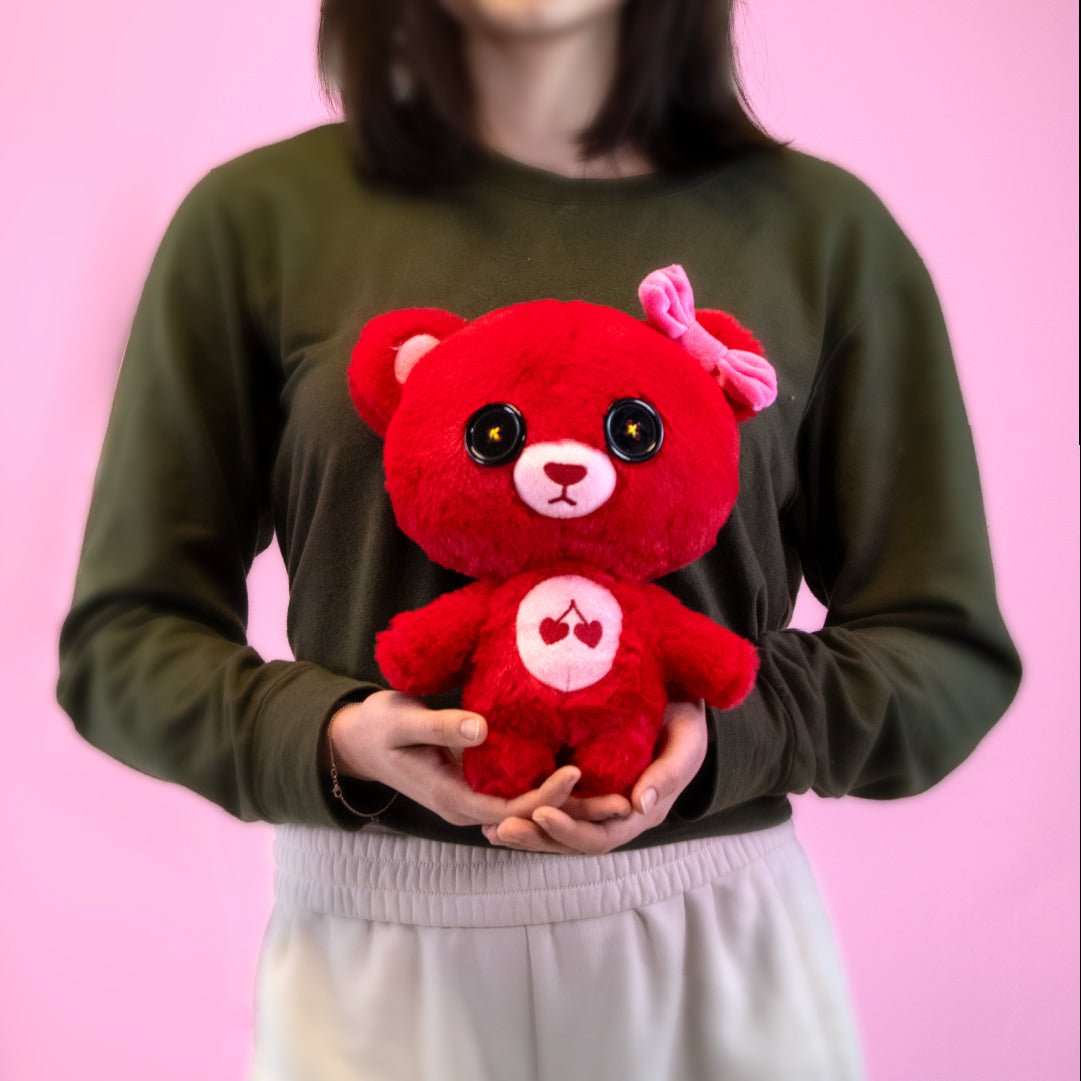 Red plush cherry bear holding a heart emblem