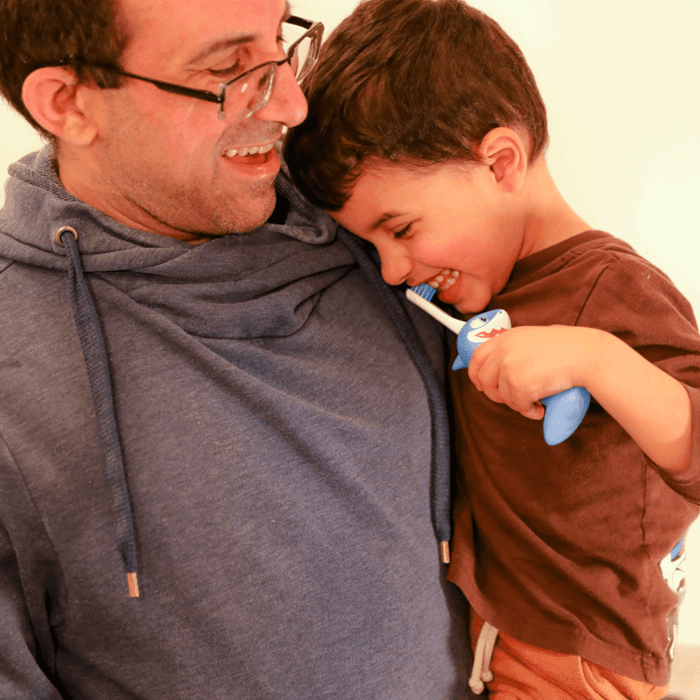 Shark kids toothbrush held by a child, blue handle with smiling shark face