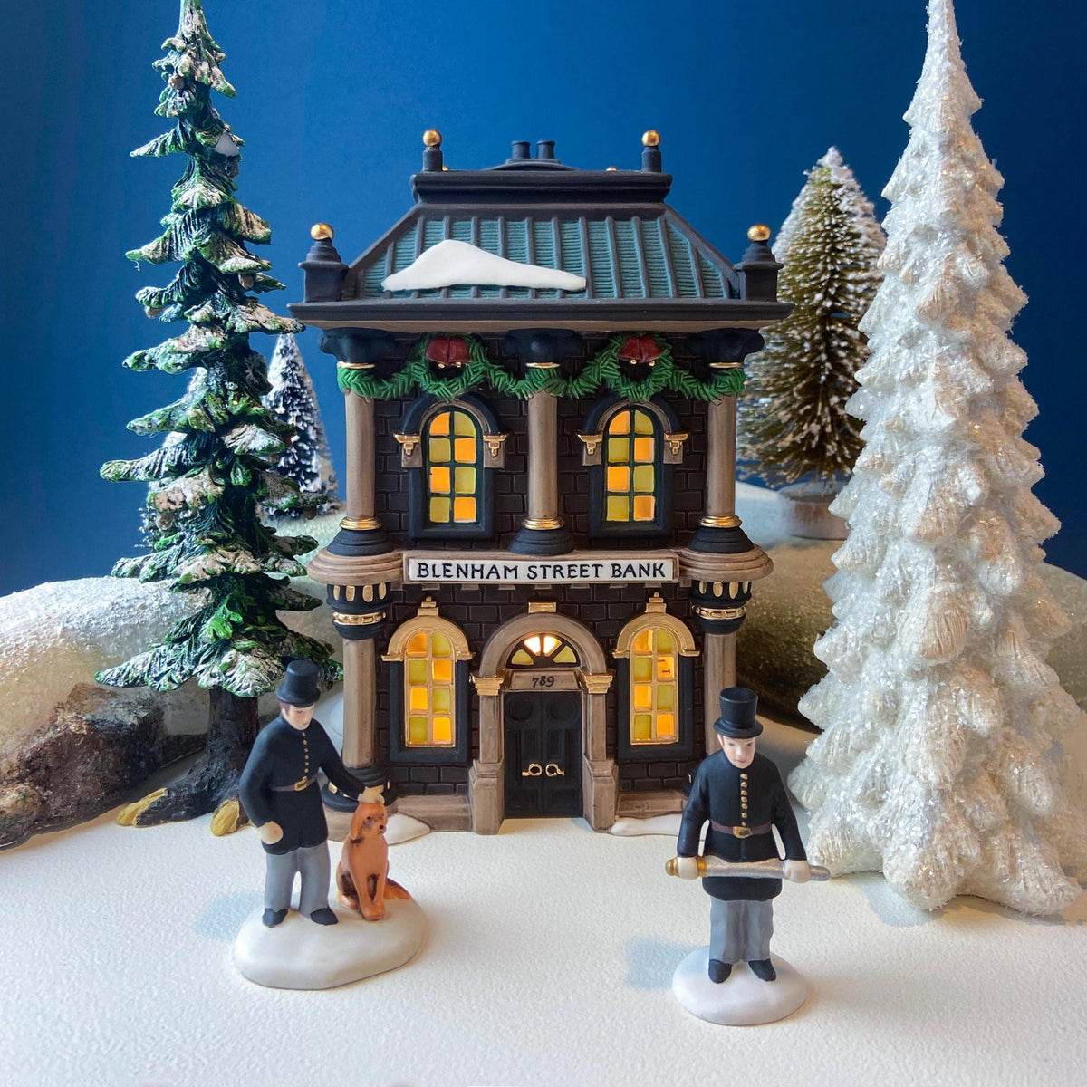 Illuminated miniature bank house with snow-covered roof and warm glowing windows