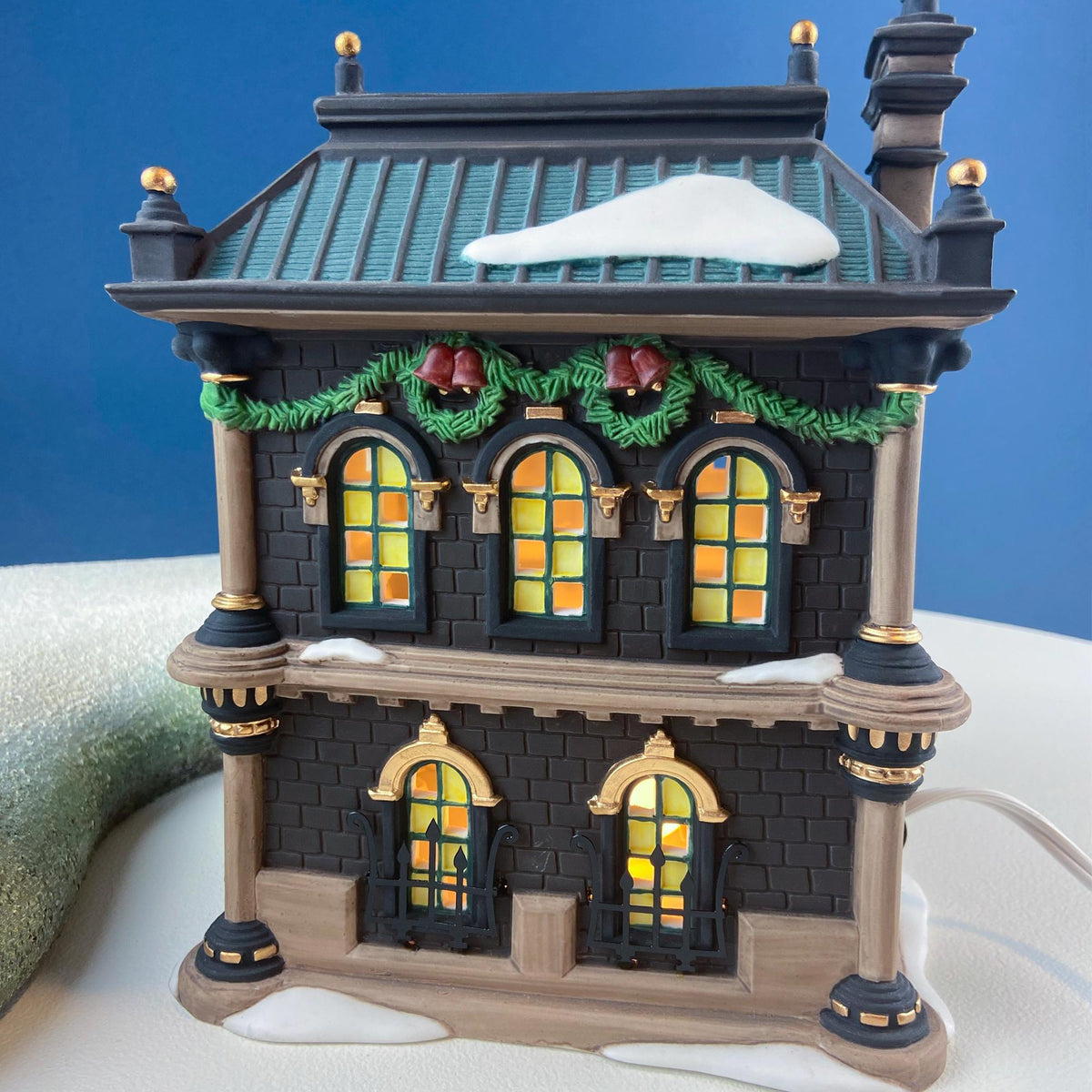 Front view of illuminated miniature bank house with lit arched windows and snow roof