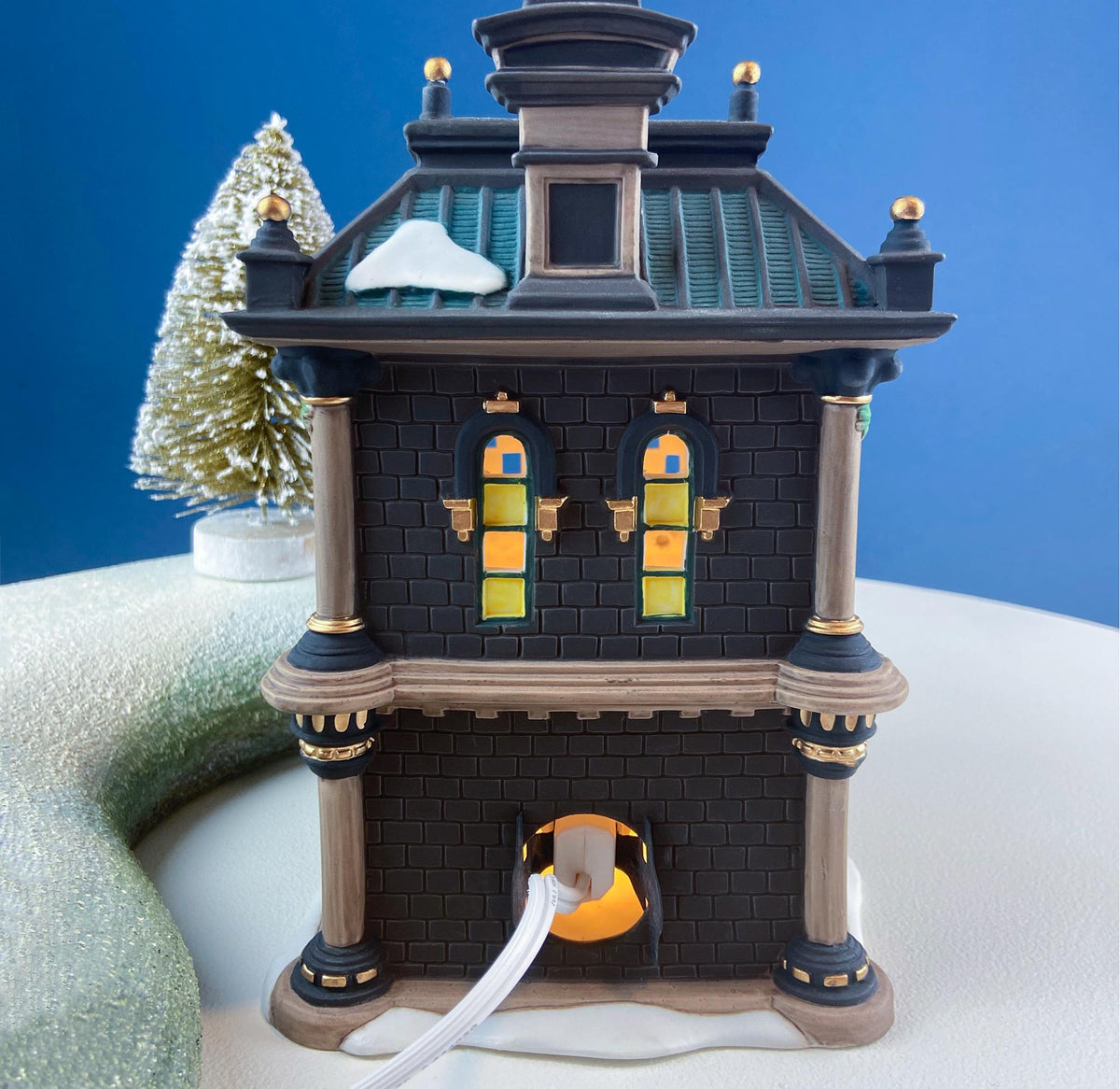 Illuminated miniature bank house with lit windows and a visible power cord