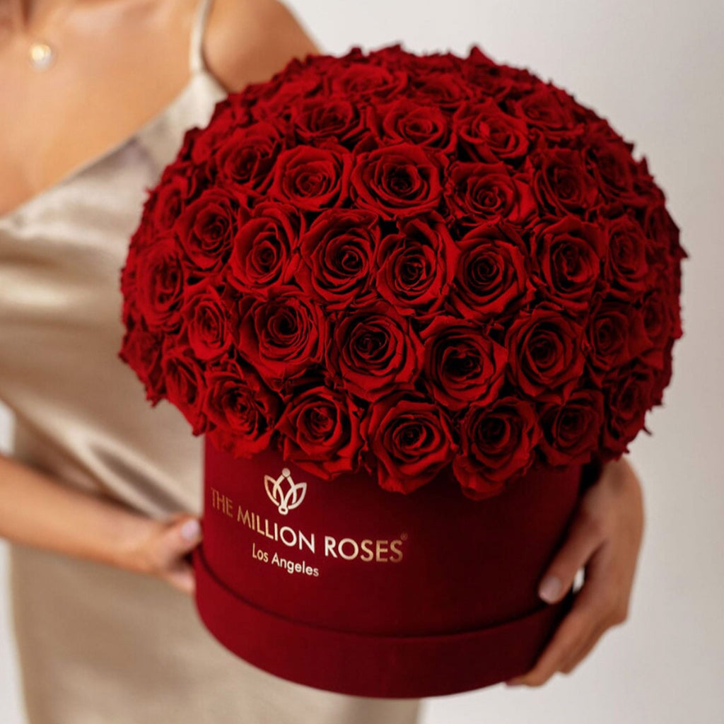 Dark-red rose bouquet in burgundy box with THE MILLION ROSES logo, held close