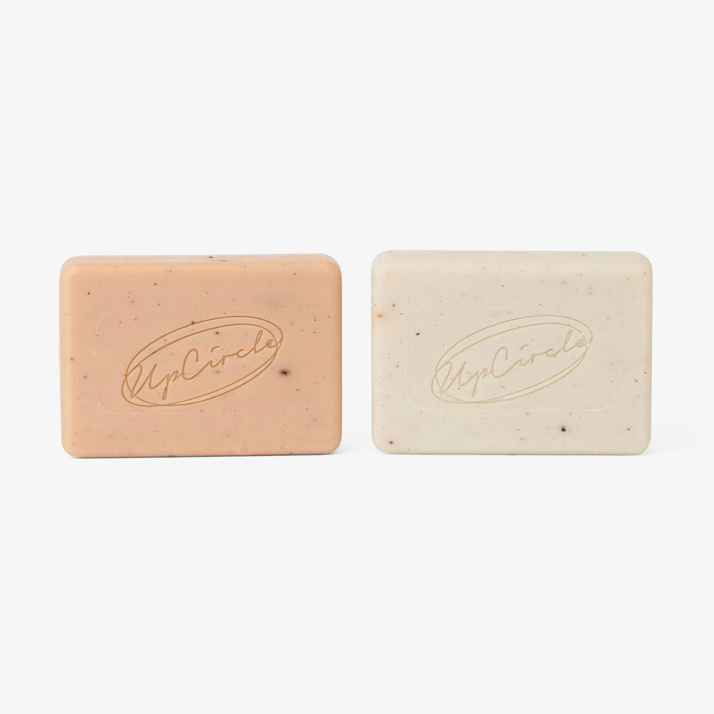 Two rectangular cleansing soap bars side by side: beige and cream with UpCircle logo
