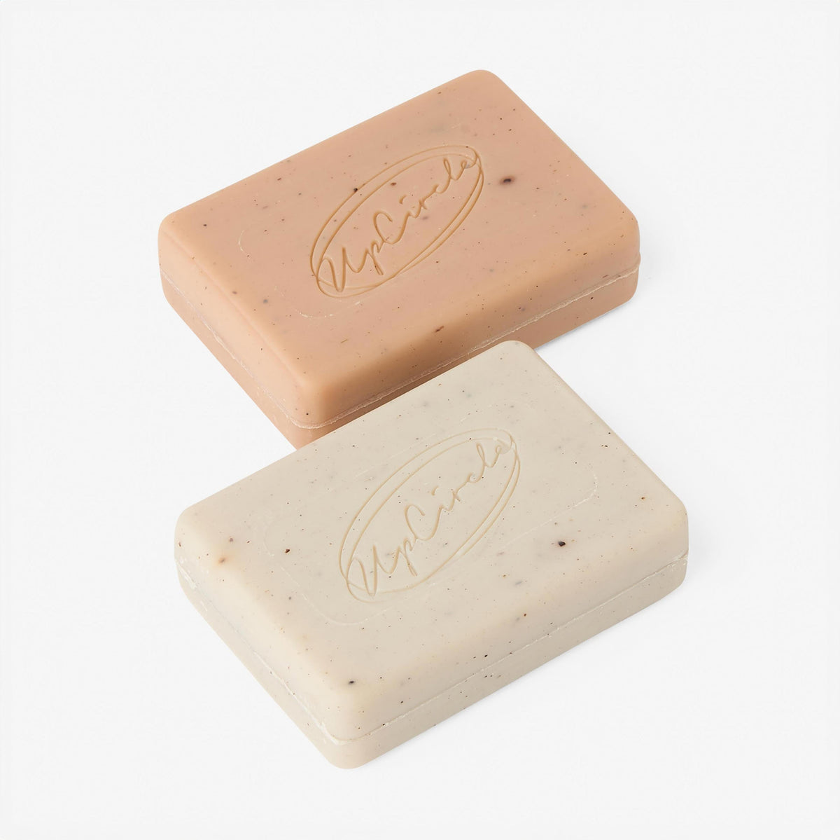 Rectangular cleansing soap bars, one beige and one cream, with UpCircle logo embossing