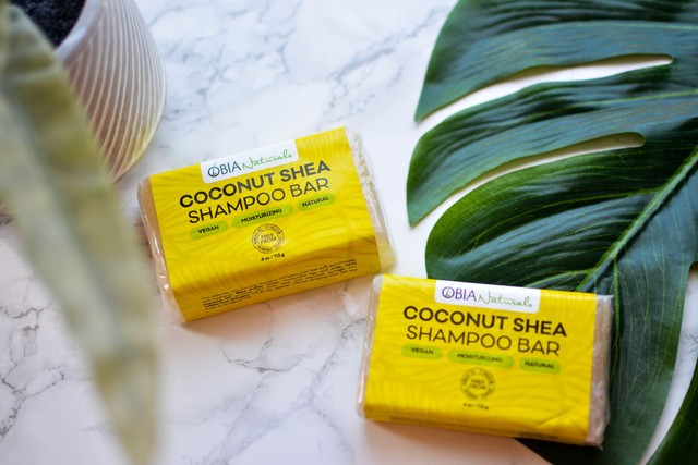 Two OBIA Naturals Coconut Shea shampoo bars on marble with green leaves