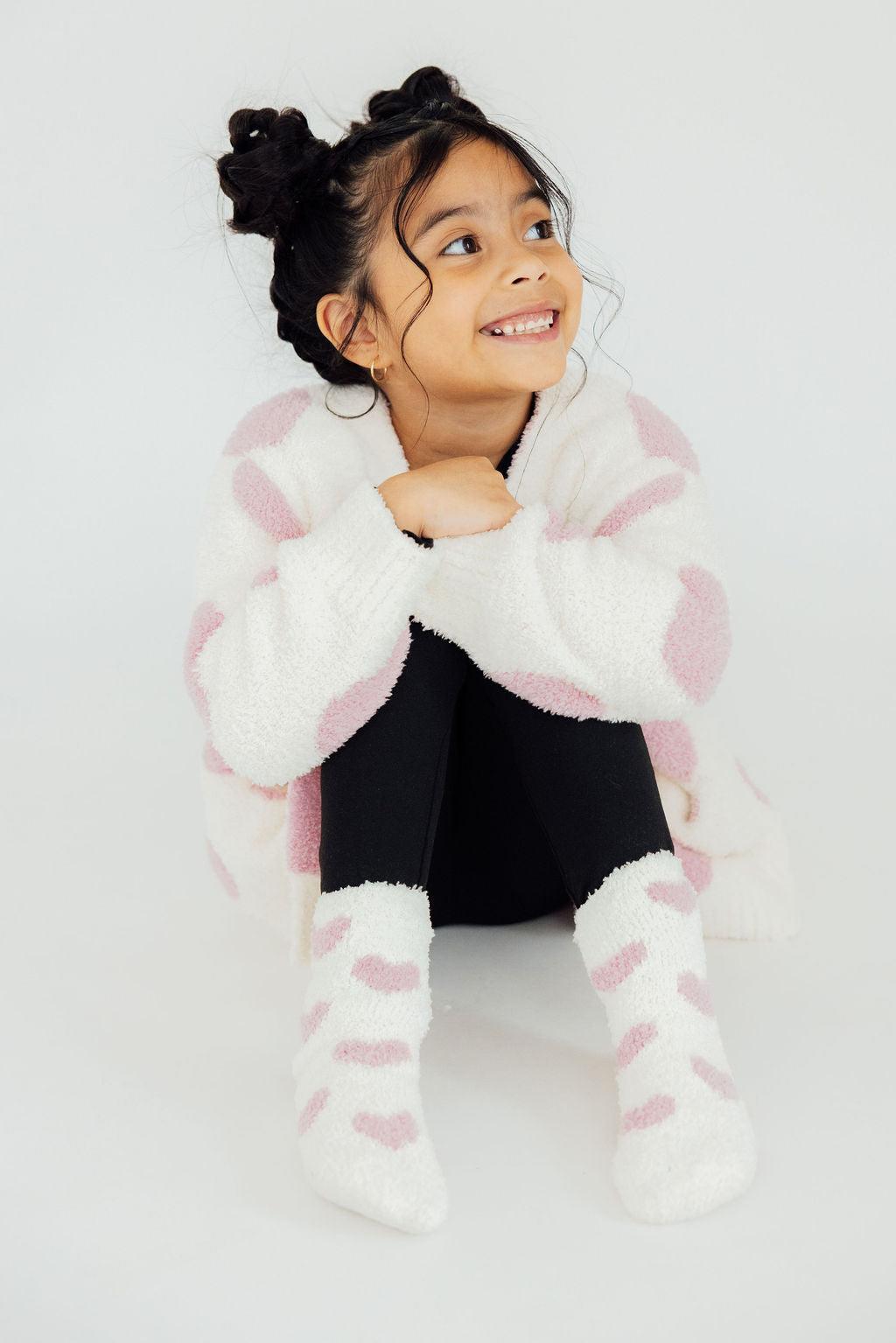 Light pink heart cozy cardigan on child, fuzzy white knit with heart pattern and long sleeves.