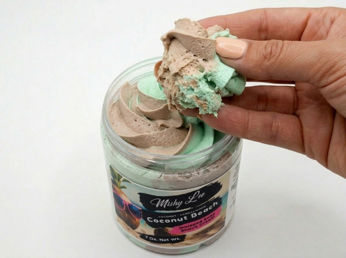 Hand holding a scoop of whipped soap and shave cream from a coconut-sand jar