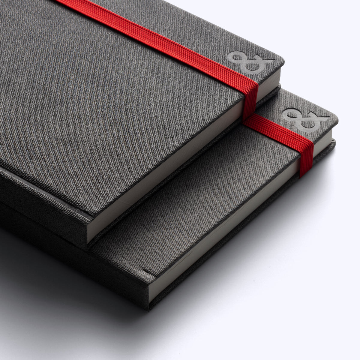 Two stacked gray habit system planners with red ribbon bands and embossed ampersand