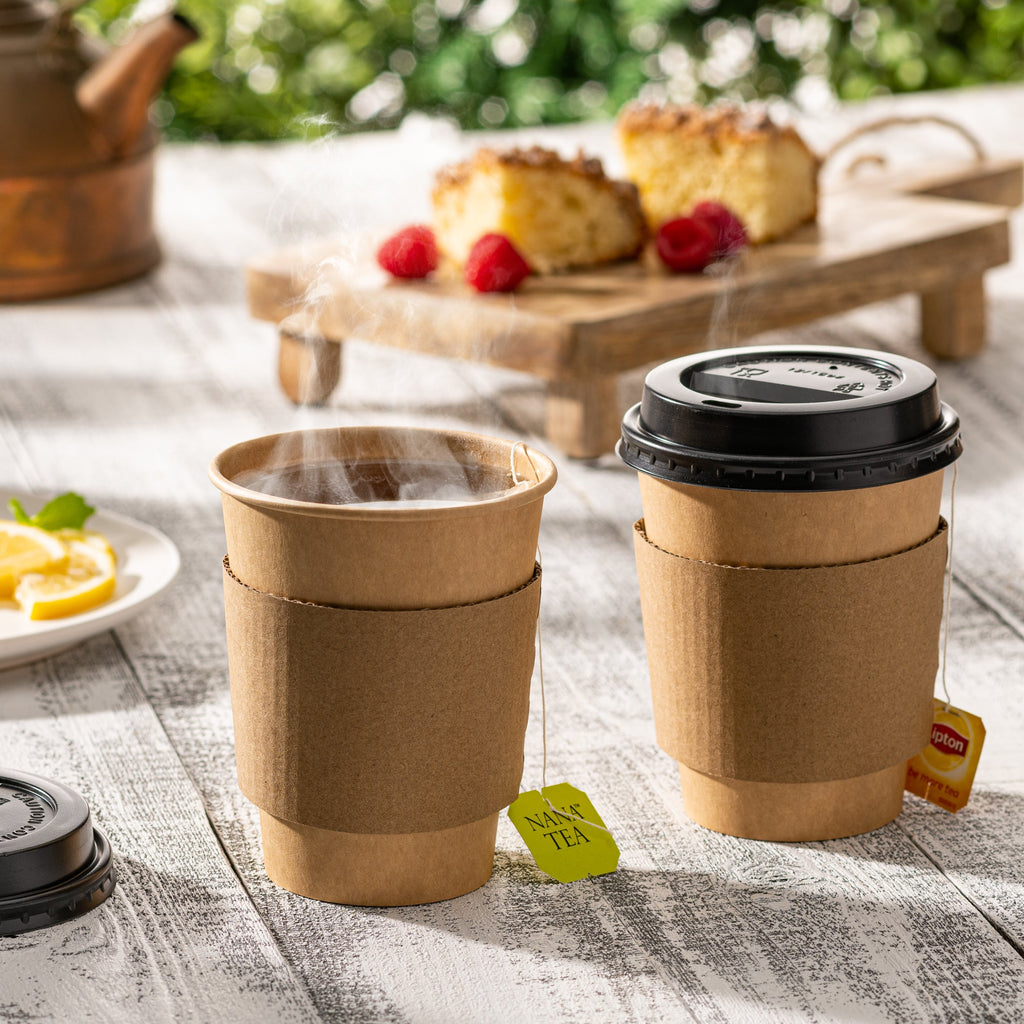 Two disposable kraft coffee cups with black lids, on a wooden table outdoors