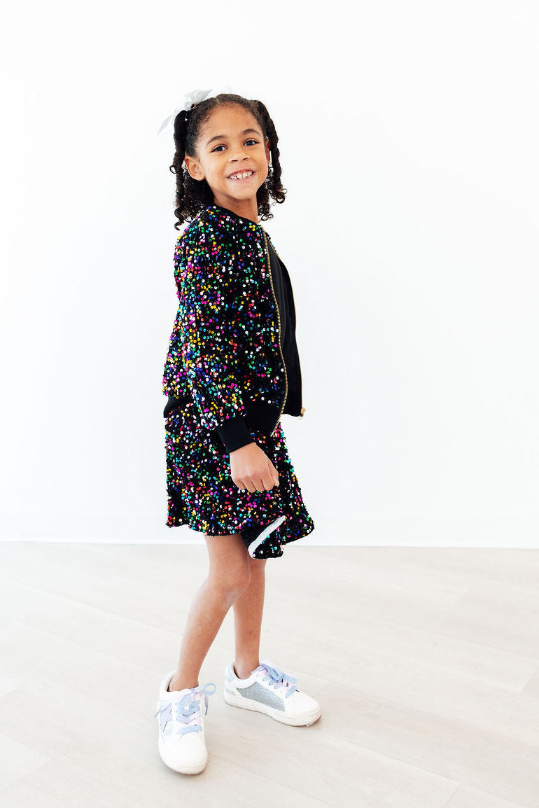 Girls' black sequin velvet jacket with multicolor confetti dots, standing full view, zip front