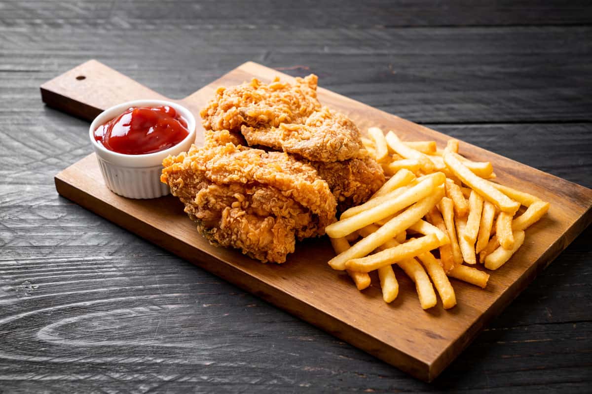 Fried chicken tenders and French fries with ketchup cup on a wooden board