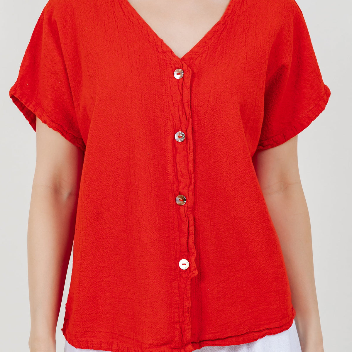 Close-up of red cotton gauze top with V-neck and round button placket