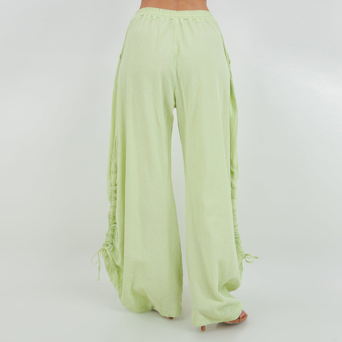 Back view of lime green cotton gauze pants with elastic waist and gathered hem ties