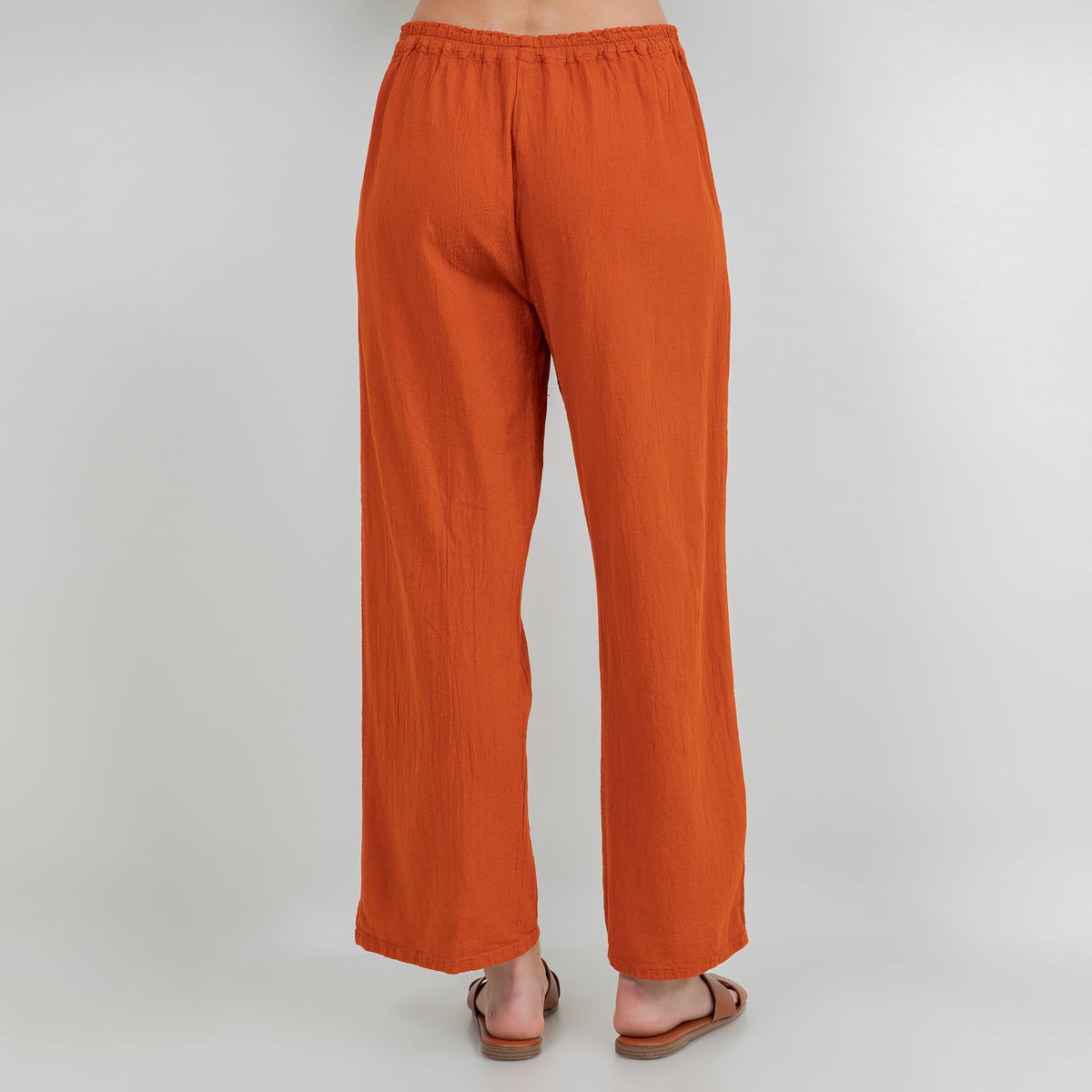 Orange cotton gauze wide-leg pants with elastic waist and ankle length; subtle side button accents