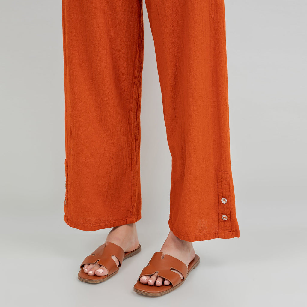 Orange cotton gauze pants, close-up of relaxed wide legs and cuff with button detail at hem