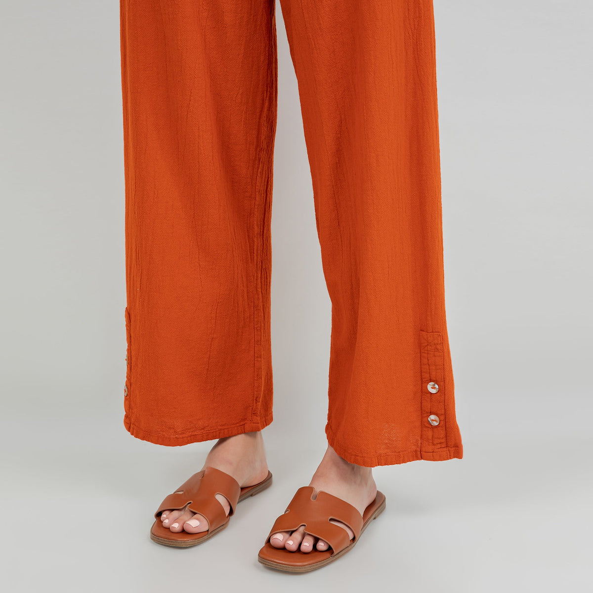 Orange cotton gauze pants, close-up of relaxed wide legs and cuff with button detail at hem