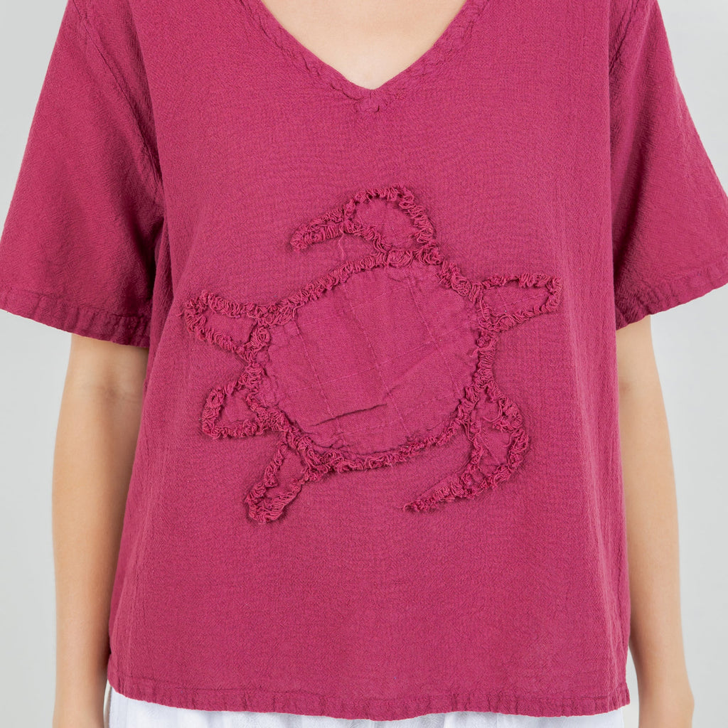 Magenta cotton gauze turtle top close-up: V-neck and embroidered turtle detail