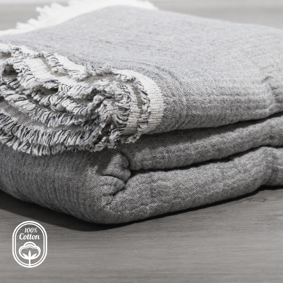 Folded grey reversible muslin coverlet with fringed trim and layered quilting texture