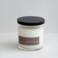 Soy candle in clear glass jar with black lid and brown label, white wax