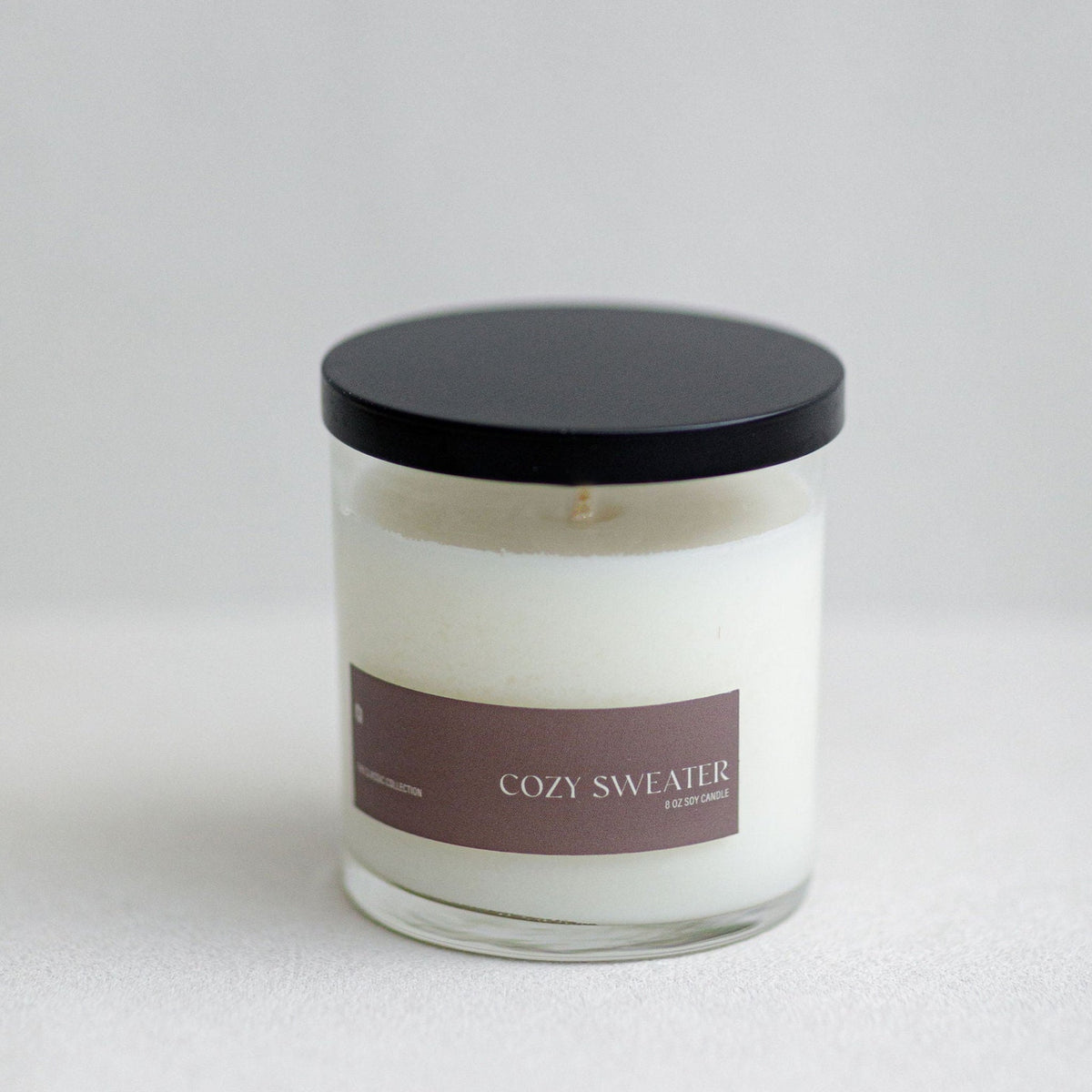 Soy candle in clear glass jar with black lid and brown label, white wax