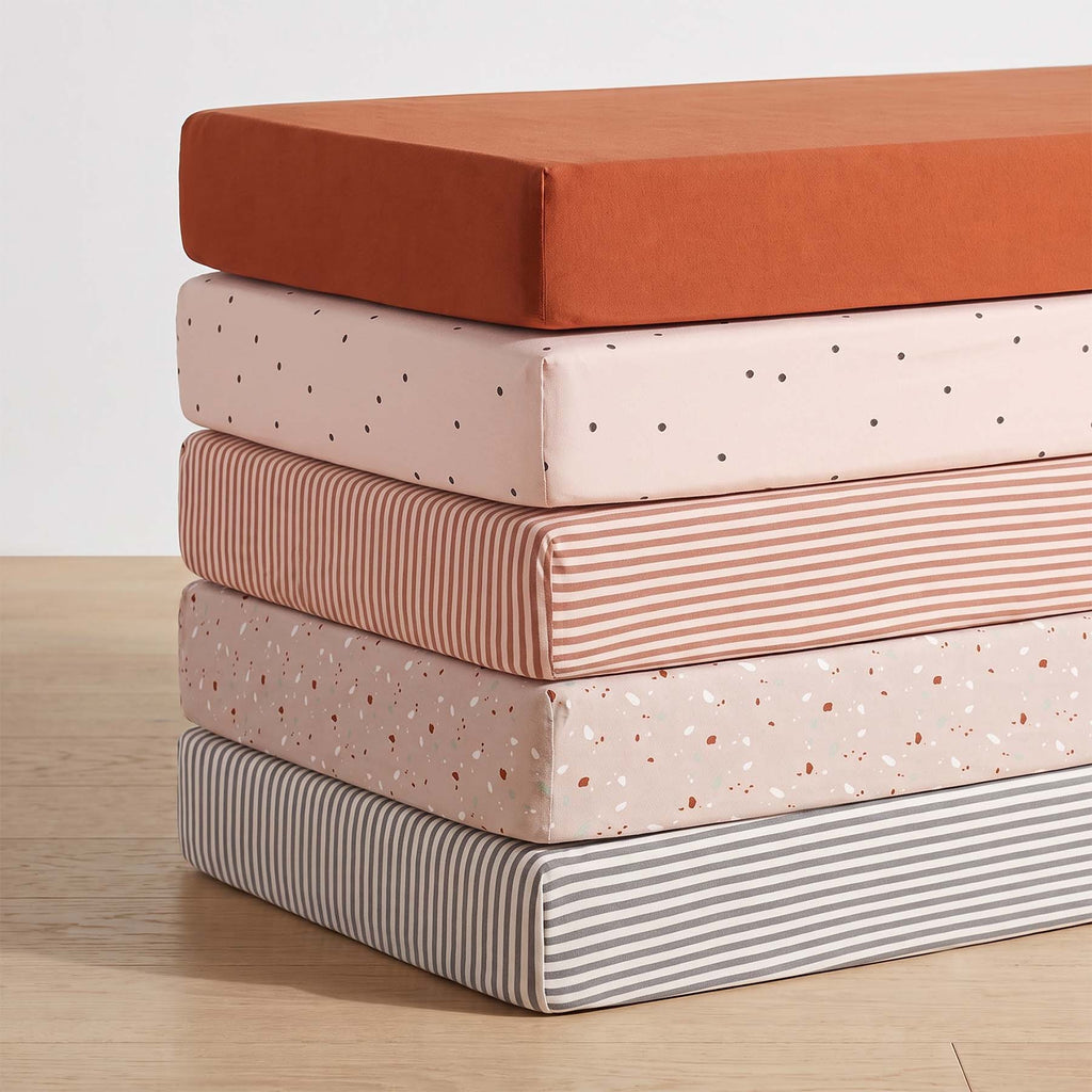 Crib sheet set with mixed prints: solid rust, dotted white, speckled and striped fabrics.