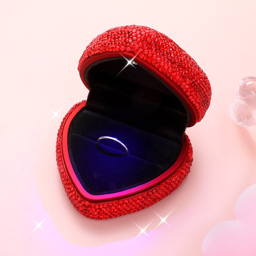 Heart-shaped ring case with red rhinestone exterior, open lid revealing blue velvet insert