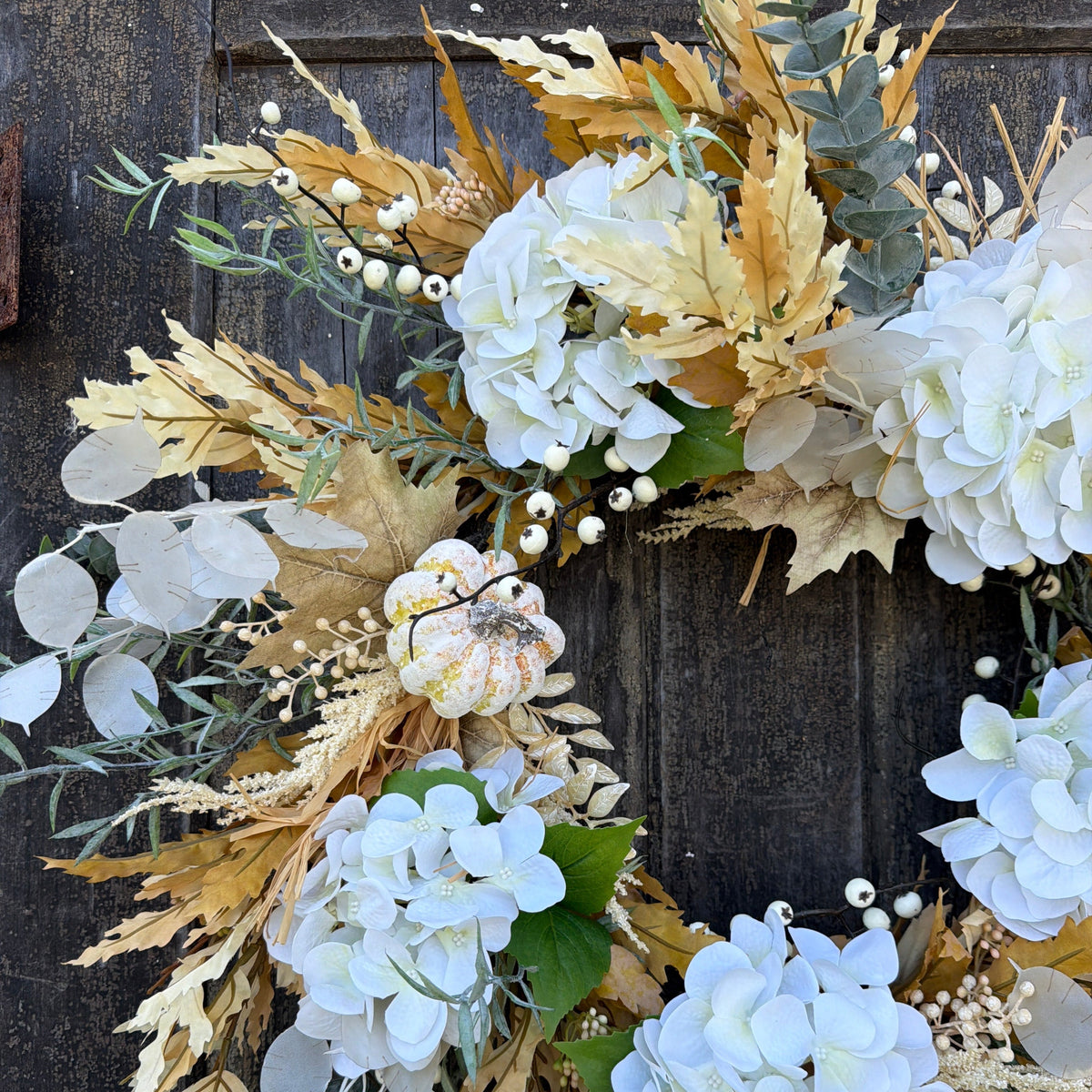 Truffle wreath featuring large white hydrangea clusters, tan foliage, eucalyptus, and round beads.