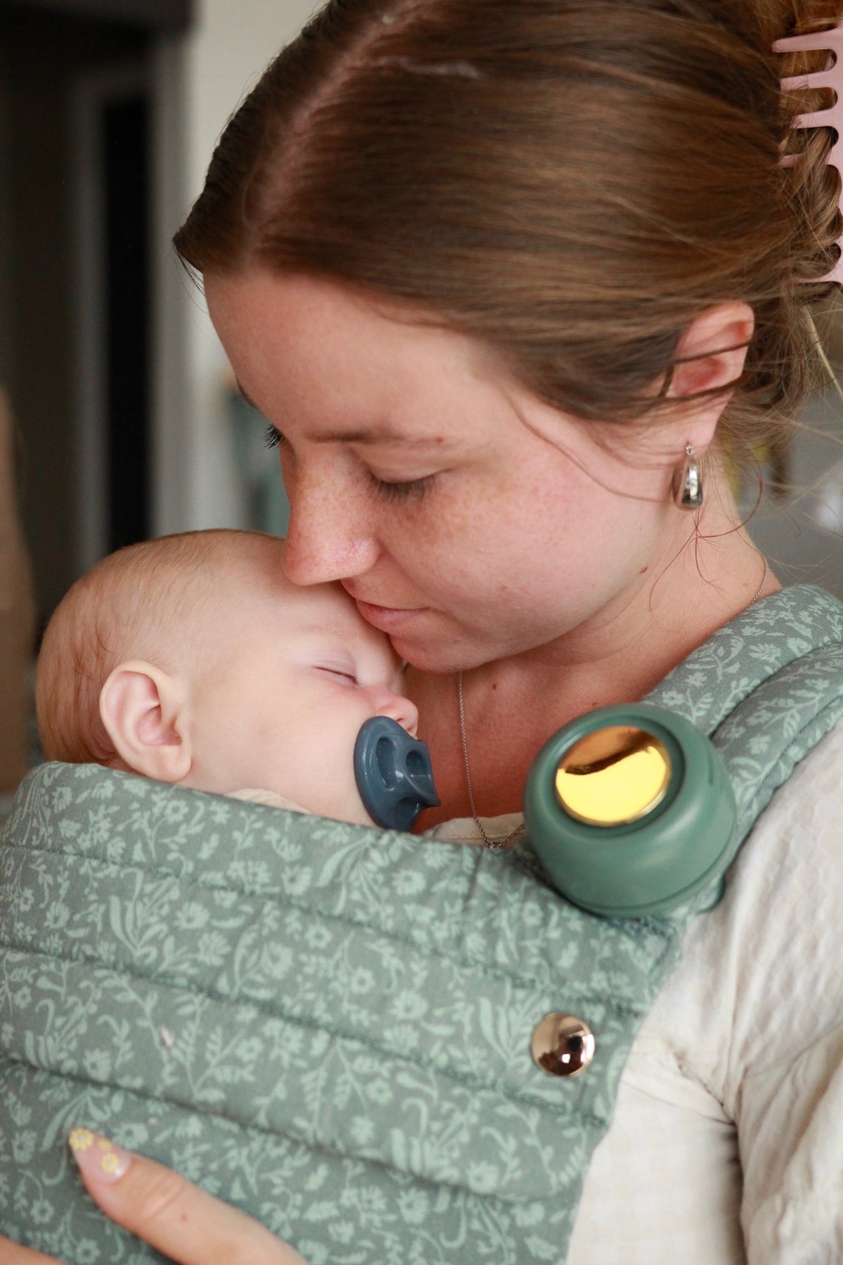 Teal floral baby carrier with pocket; close-up of parent cuddling newborn