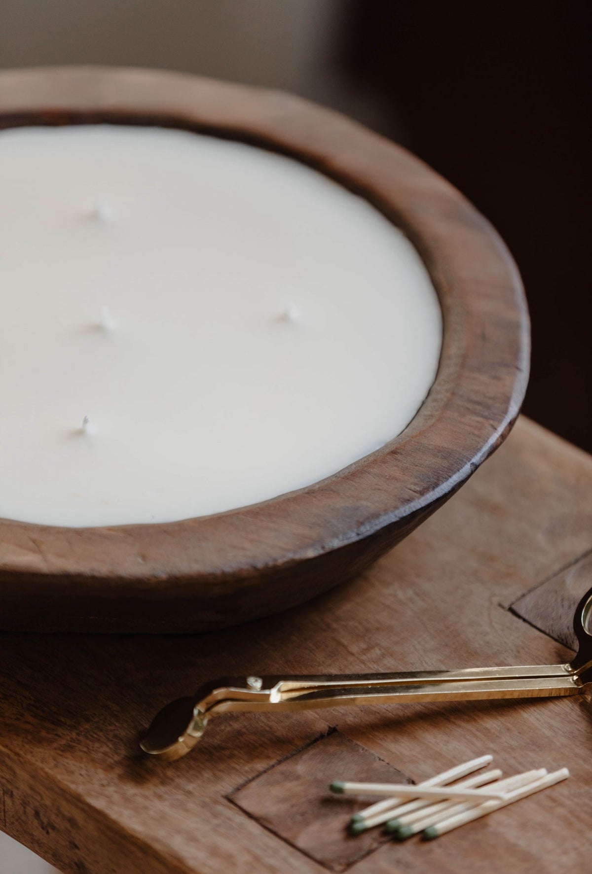 Wooden bowl candle close-up with creamy white wax and wick tools beside it