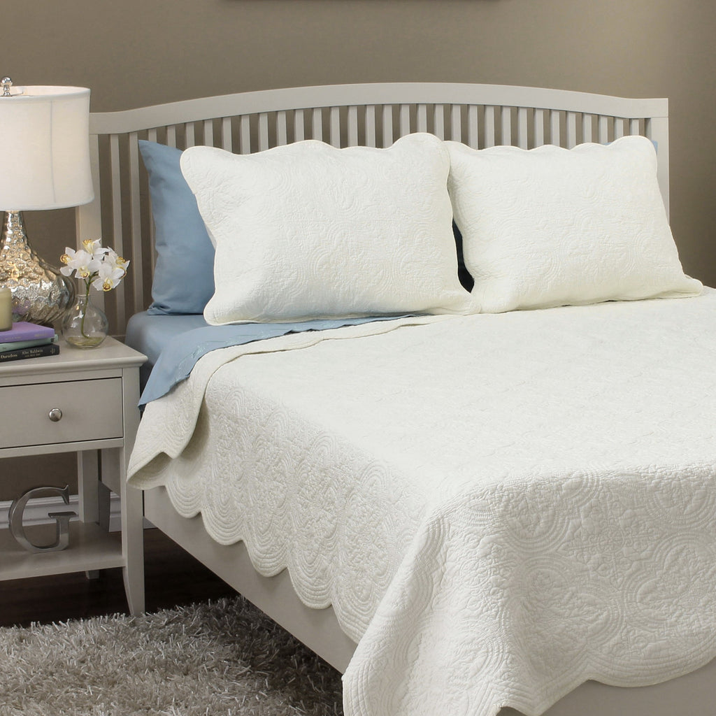 Ivory quilt set on bed with two matching pillow shams and scalloped quilt edge