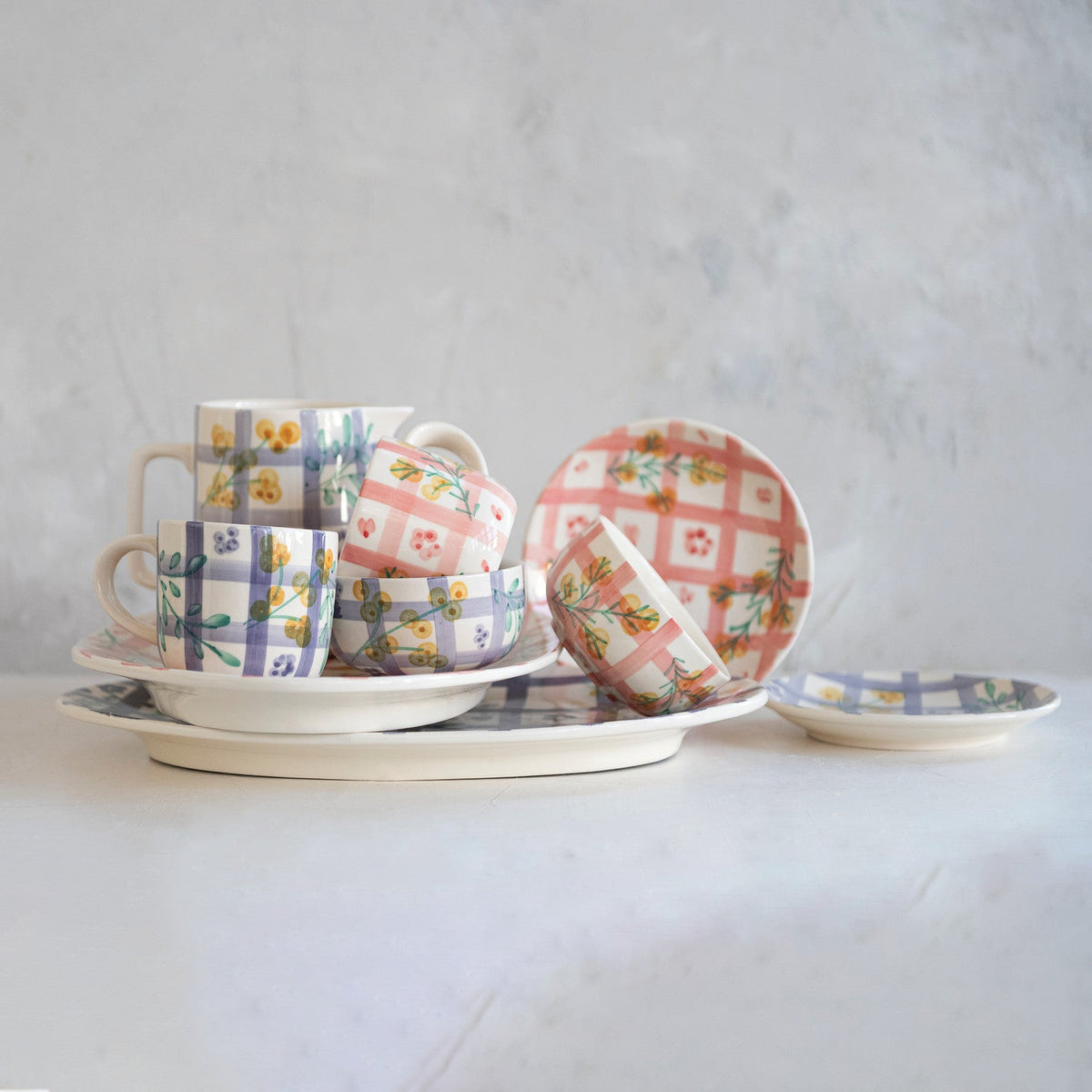 Ceramic mug set on saucers with plaid and botanical motifs, plus matching plates