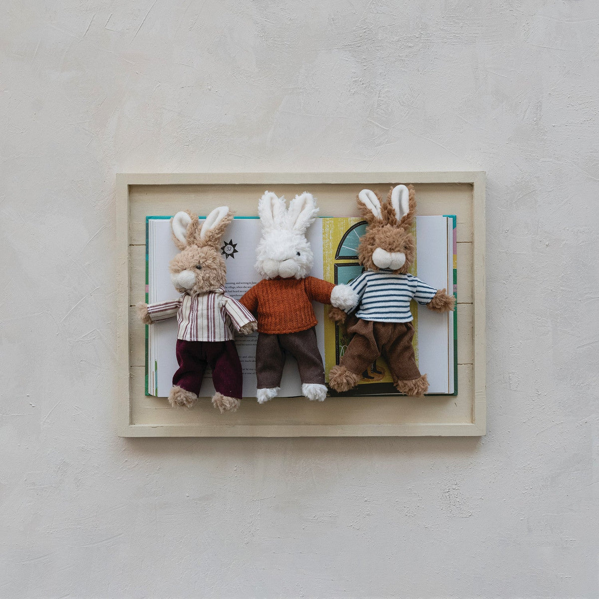 Framed plush bunny toy set with three bunnies wearing striped shirts and sweaters.