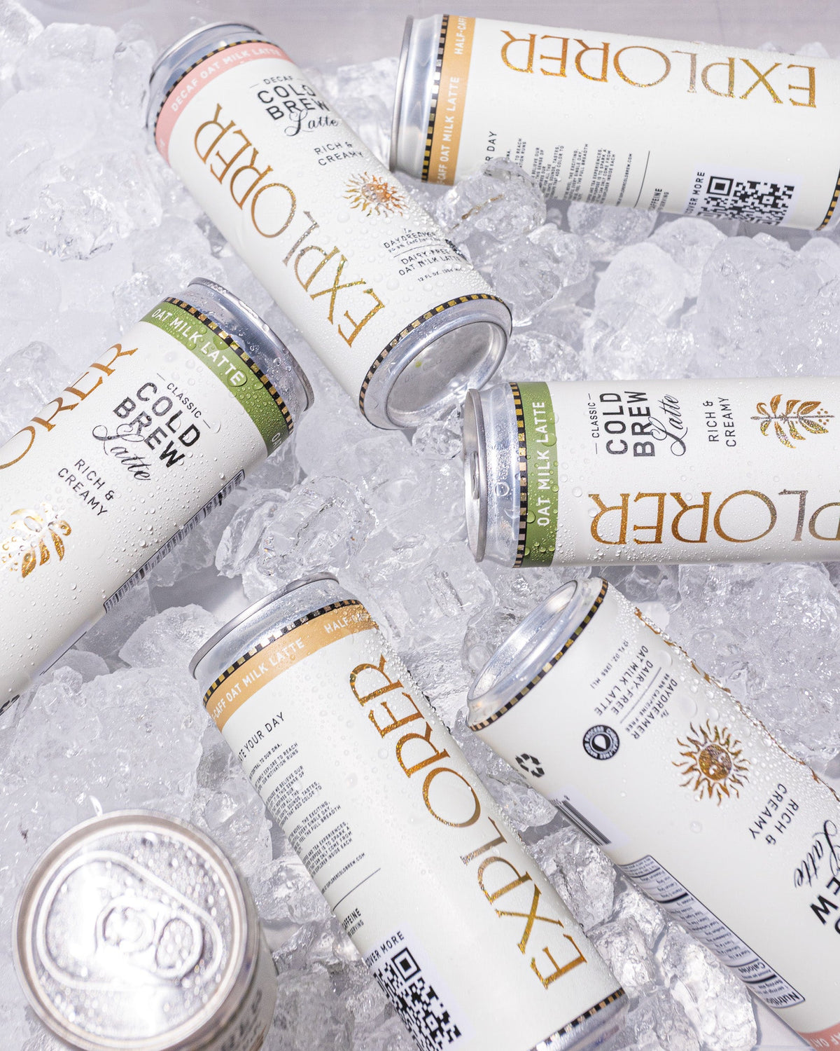 Multiple decaf cold brew oat latte cans on ice, white cans with gold branding