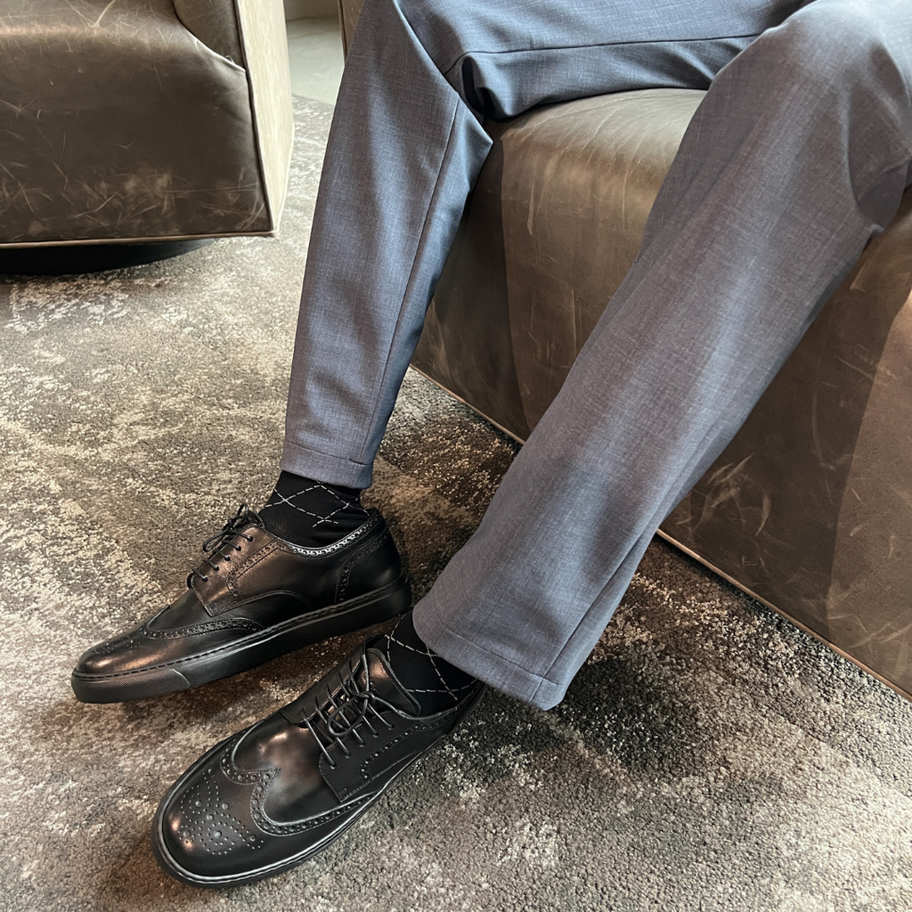 Black wingtip lace-up dress shoes worn with light trousers